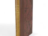 an old book with a red cover sitting on top of a white surface