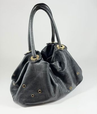 sac à main en cuir noir avec des anses cloutées dorées sur fond blanc