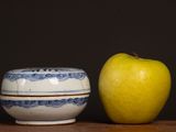 a yellow apple next to a blue and white bowl on a table