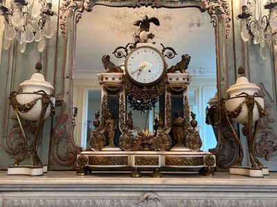 une horloge posée sur une cheminée, devant un miroir