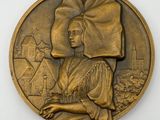 bronze medal depicting a woman with a hat on her head