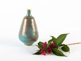 a blue vase and a pink flower on a white surface