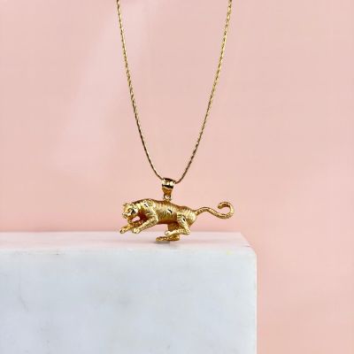 un collier représentant un lion en or posé sur un bloc de marbre, sur fond rose