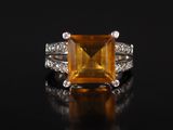une bague sertie d'un saphir orange et de diamants, posée sur un fond noir