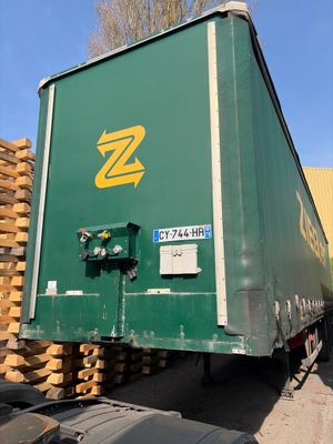un gros camion vert garé à côté d'un tas de bois