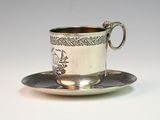 a silver cup and saucer sitting on a saucer