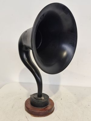 un vieux gramophone noir posé sur un socle en bois, lui-même posé sur une surface blanche