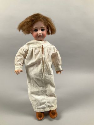une poupée à l'ancienne, aux cheveux bruns et vêtue d'une robe blanche