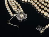 a close up of a necklace with pearls and a flower broocher
