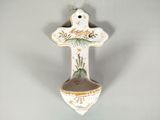 une croix en céramique accrochée au mur, sur laquelle est représenté un oiseau