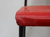 a close up of a red chair with peeling paint on it
