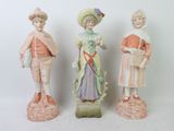 three porcelain figurines of people dressed in different outfits