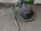 un aspirateur vert et noir posé par terre, à côté d'un mur de briques blanches