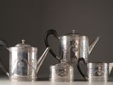 a silver tea set on a table next to a cup and saucer
