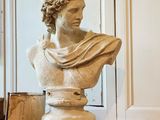 un buste d'homme assis sur un socle, à côté d'une bougie allumée