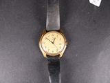 an image of a gold watch with a black strap on a black surface