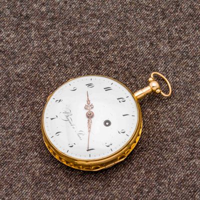 une montre de poche en or posée sur une surface marron
