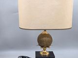 une lampe dorée avec un pied noir et un abat-jour beige