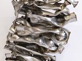 sculpture en argent représentant une grande pile d'objets métalliques posée sur une surface blanche