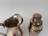 a silver pitcher and a silver shaker on a white table