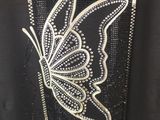 the back of a black shirt with a butterfly embroidered on it