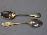 two silver spoons sitting on top of a table next to each other