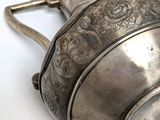 a silver pot with a handle on a white surface