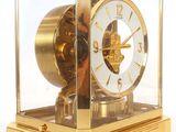 a gold clock in a glass case on a white surface