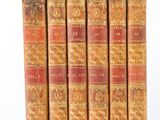 six old books are lined up in a row on a white surface
