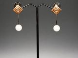 a pair of gold and pearl earrings on a black stand