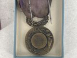 purple ribbon in a blue box with a gold medal on top of it