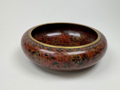un bol rouge bordé d'or posé sur une surface blanche