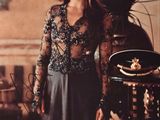 une image représentant une femme en robe longue, debout devant une table