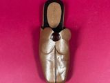 gold ballet shoes on a pink surface with a black bow