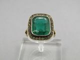 a close up of a ring with a green stone surrounded by diamonds