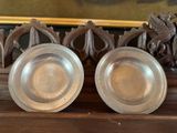two silver plates sitting on top of a wooden shelf