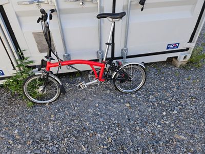 a red bike that is parked next to a white container