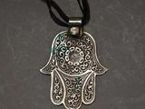 a silver hamsa hand pendant with a black cord on a gray background