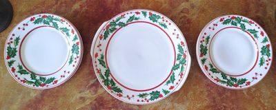 three plates with holly leaves and red rims sit on a table