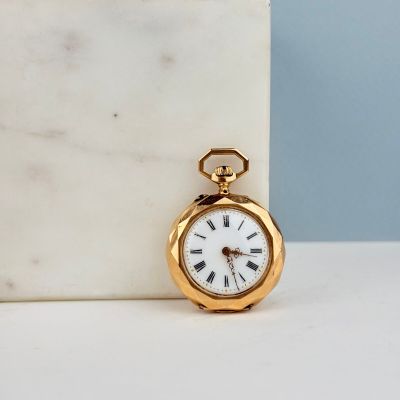 une petite montre de poche en or posée sur un bloc de marbre