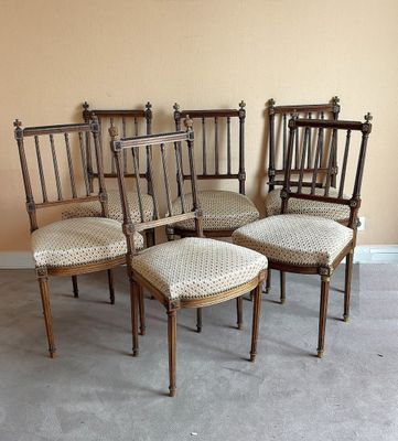 six chaises anciennes aux assises rembourrées sont alignées contre un mur beige