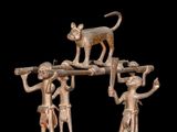 three bronze figurines of people and a cat on top of a pole