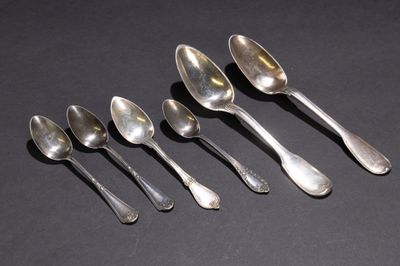 six cuillères en argent sont alignées sur une surface noire