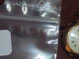 une petite montre de poche en or posée à côté d'un sac en plastique