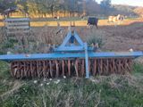 a blue plow in the middle of a field with cows in the background