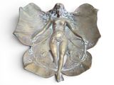 une sculpture métallique représentant une femme ailée posée sur une feuille