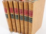 six vieux livres sont empilés sur une surface blanche