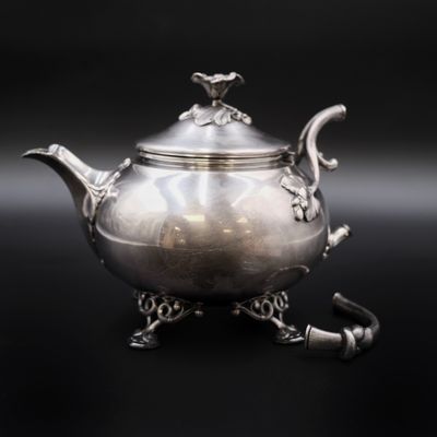 une théière ancienne en argent posée sur un socle, sur fond noir