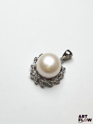 un gros plan d'un pendentif en perle blanche posé sur une surface blanche