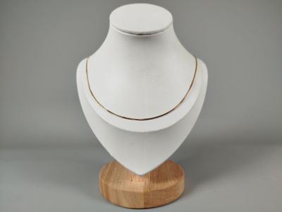 mannequin blanc avec une chaîne en or, posé sur un socle en bois